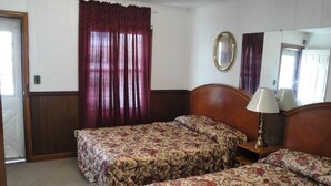 Ein Hotelzimmer mit zwei Einzelbetten, einem hölzernen Kopfteil, einem Nachttisch mit Lampe, einem Spiegel und einem Fenster mit Vorhängen.