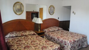 Ein Hotelzimmer mit zwei Einzelbetten, einem hölzernen Kopfteil, einem Nachttisch mit Lampe und zwei gerahmten Bildern an der Wand.