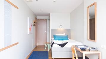 A modern hotel room with a bed, bedside table, chair, and a desk with a telephone.