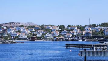 En kuststad med hus längs vattnet, en brygga och en fyr i bakgrunden.
