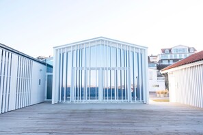 Un bâtiment moderne à la façade blanche et aux grandes fenêtres, situé sur une terrasse en bois offrant une vue sur la mer.