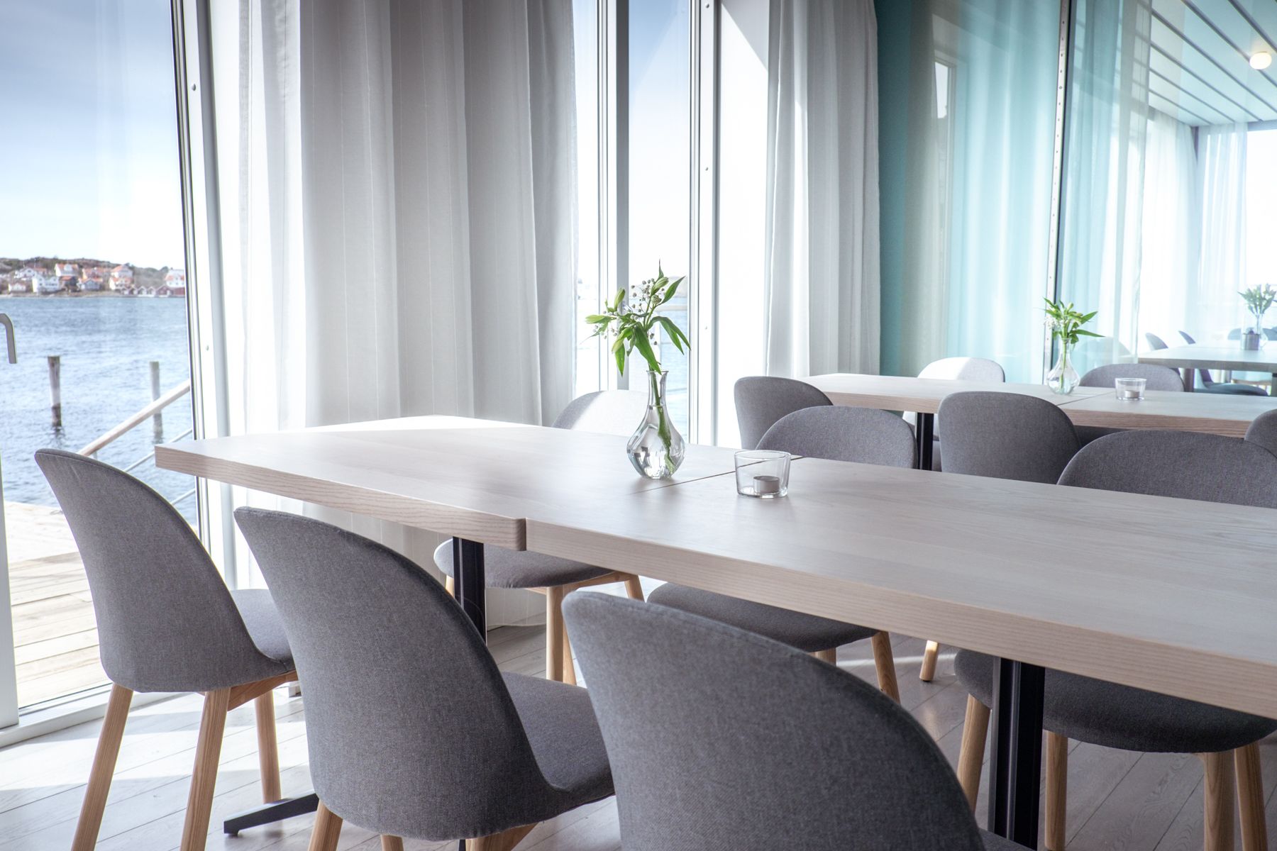 A modern dining area with a long table, grey upholstered chairs, and a vase with flowers.