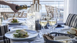 Een eettafel gedekt met borden eten, glazen witte wijn en een fles die wordt ingeschonken.