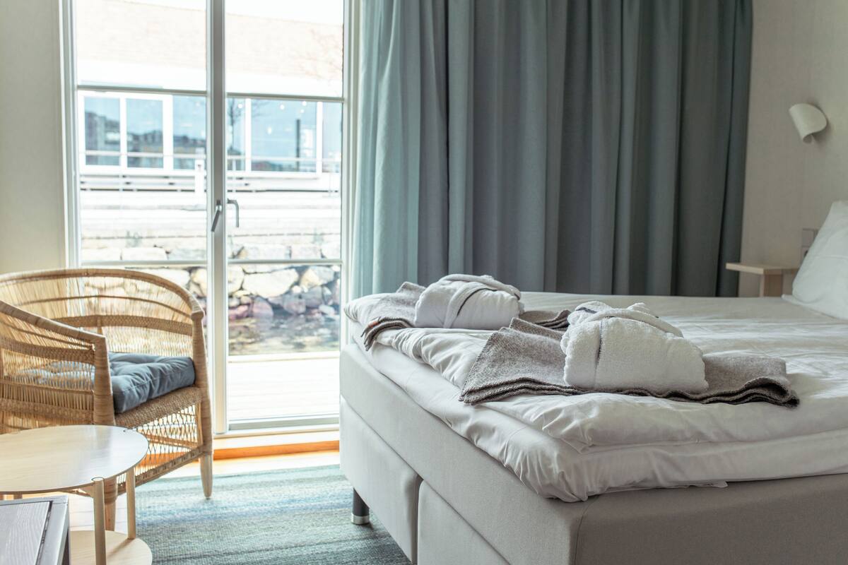 Ein Hotelzimmer mit Bett, Korbsessel, Tisch und Blick ins Freie.