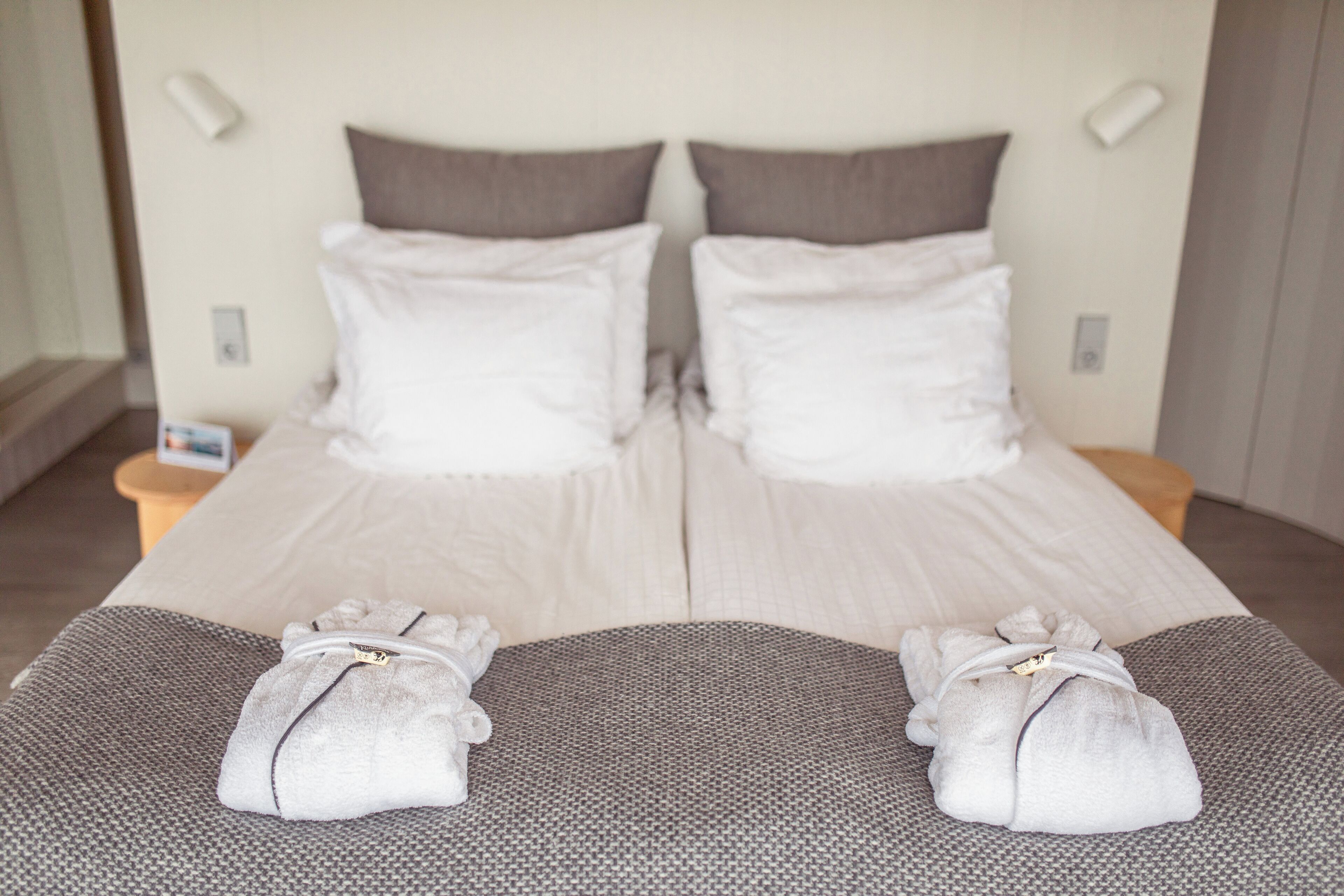 A double bed with white and gray bedding, two towels on the bed, and bedside lamps.