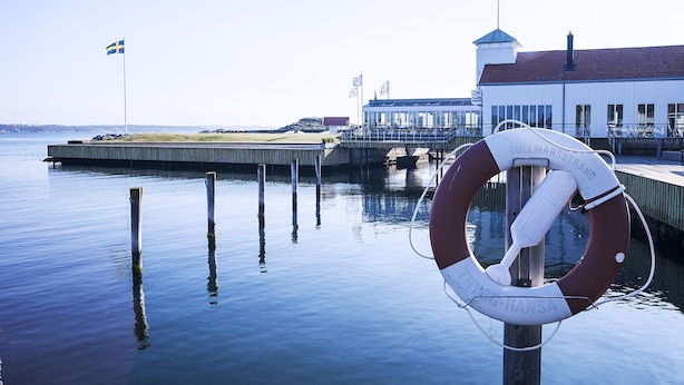 Reddingsboei bevestigd aan een houten paal aan een rustig waterfront, met een gebouw op de achtergrond.