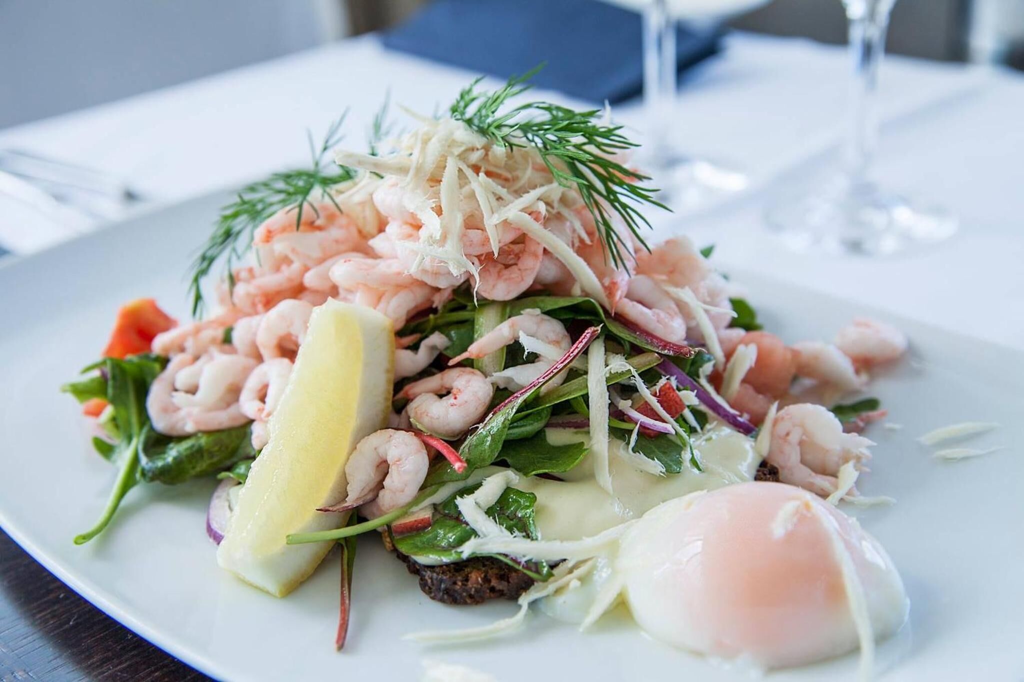 Ein Teller Garnelensalat mit Grünzeug und einem pochierten Ei.