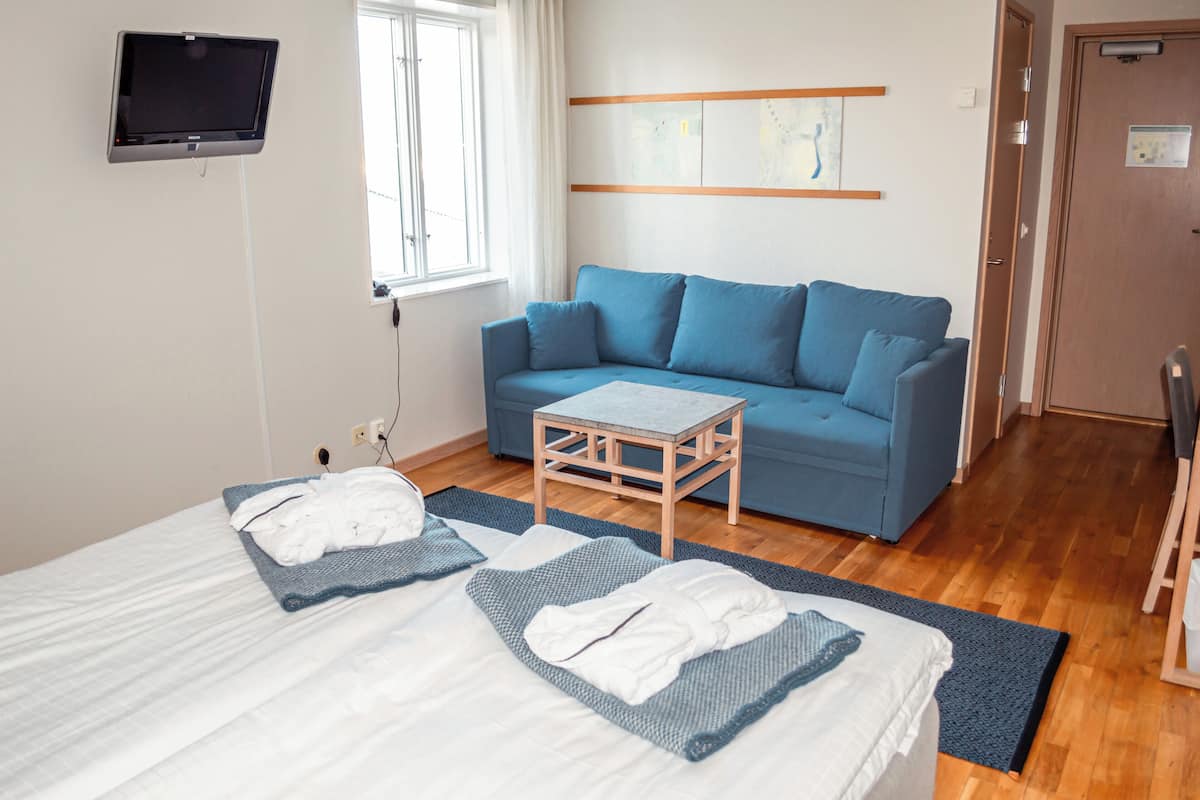 Ein Hotelzimmer mit einem Bett, einem blauen Sofa, einem kleinen Holztisch und einem an der Wand befestigten Fernseher.