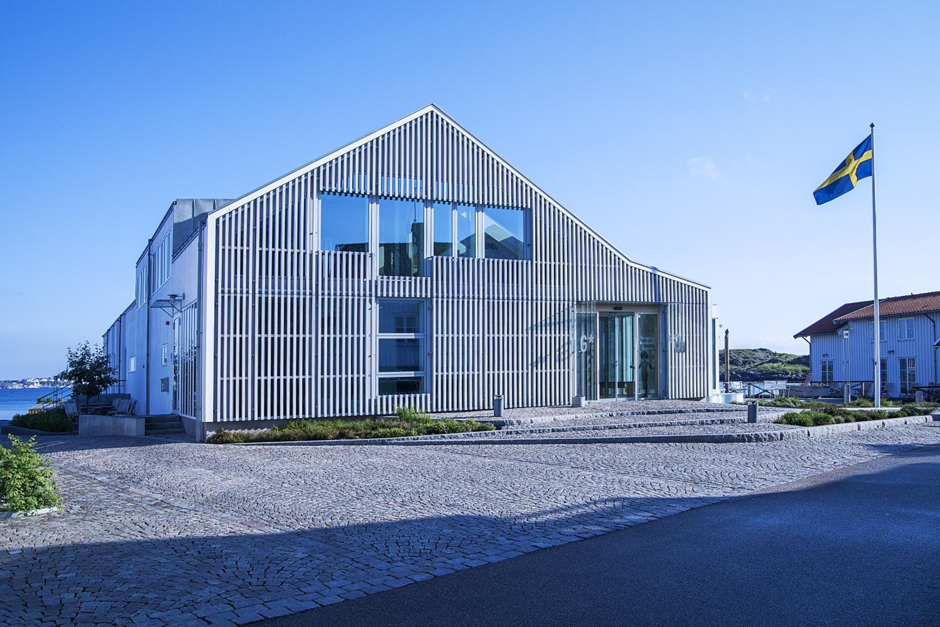 Un bâtiment moderne, doté d’un toit en pente et de grandes fenêtres, situé dans une rue pavée, avec un drapeau en arrière-plan.