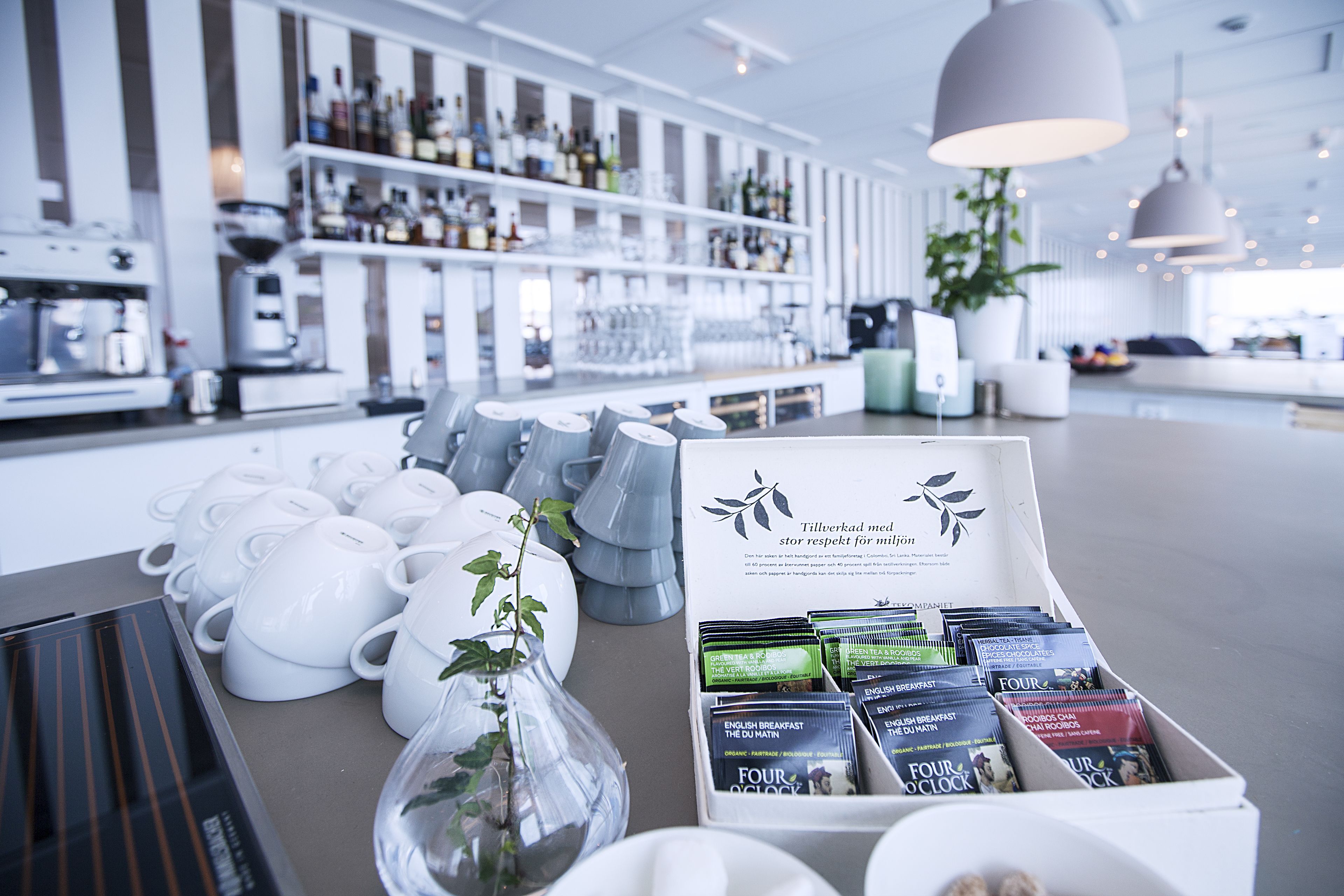 A modern bar area with white mugs, a coffee machine, and a display of coffee packets.