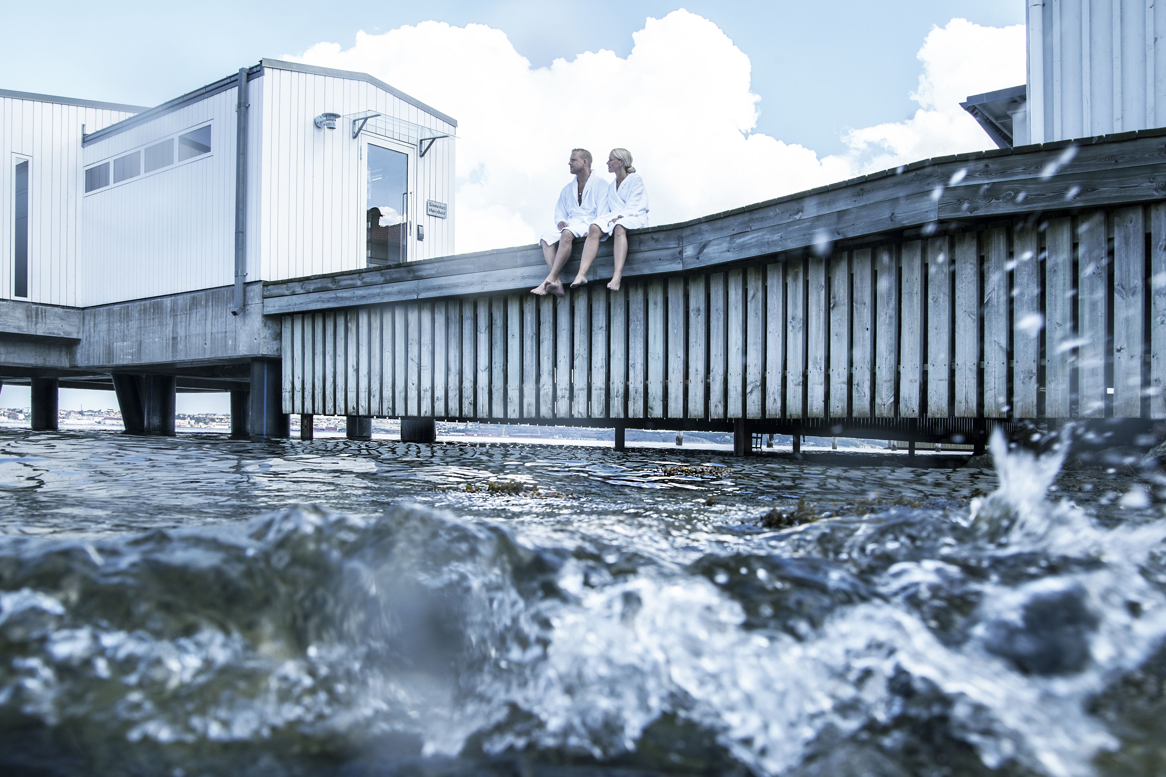 A wooden pier extending over a body of water with two individuals sitting on it.