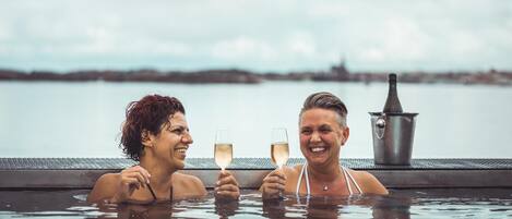 Dos personas en un jacuzzi con vista a un cuerpo de agua y una costa lejana.