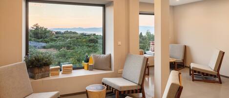 Una sala de estar moderna con un amplio ventanal que ofrece vistas a un paisaje pintoresco, con varias opciones de asientos cómodos y una pequeña mesita.