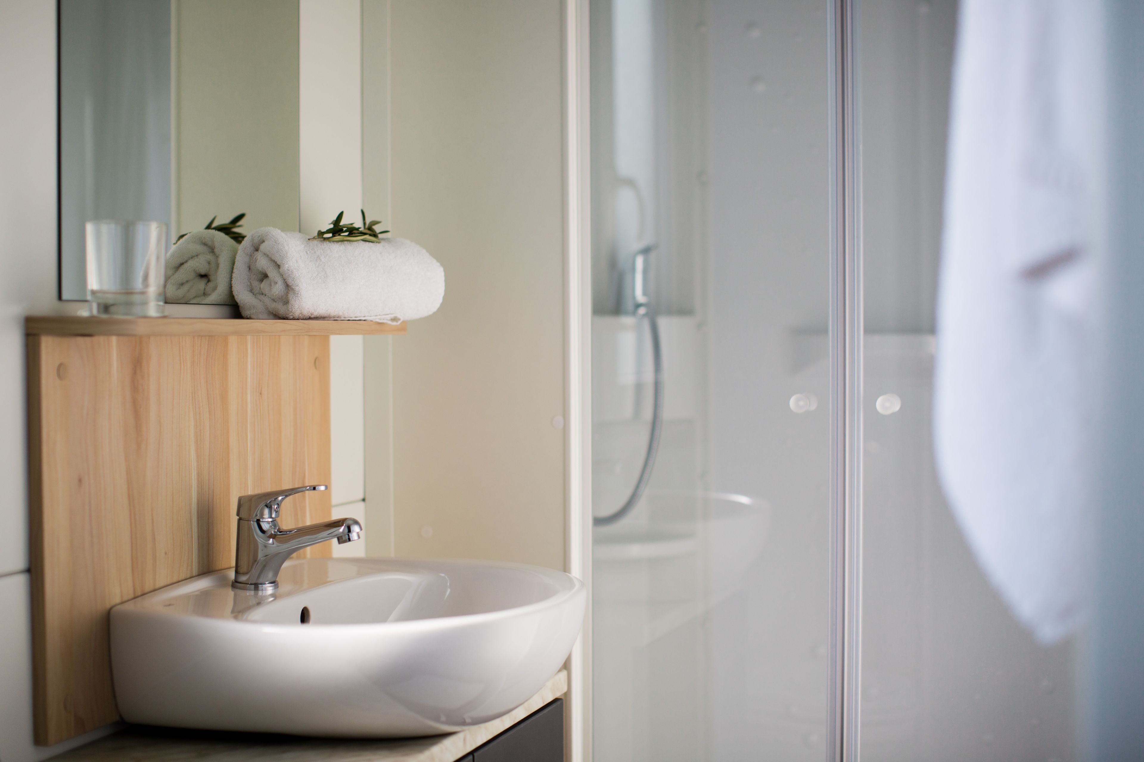 A bathroom with a white sink, a wooden vanity, a mirror, and a glass shower enclosure.