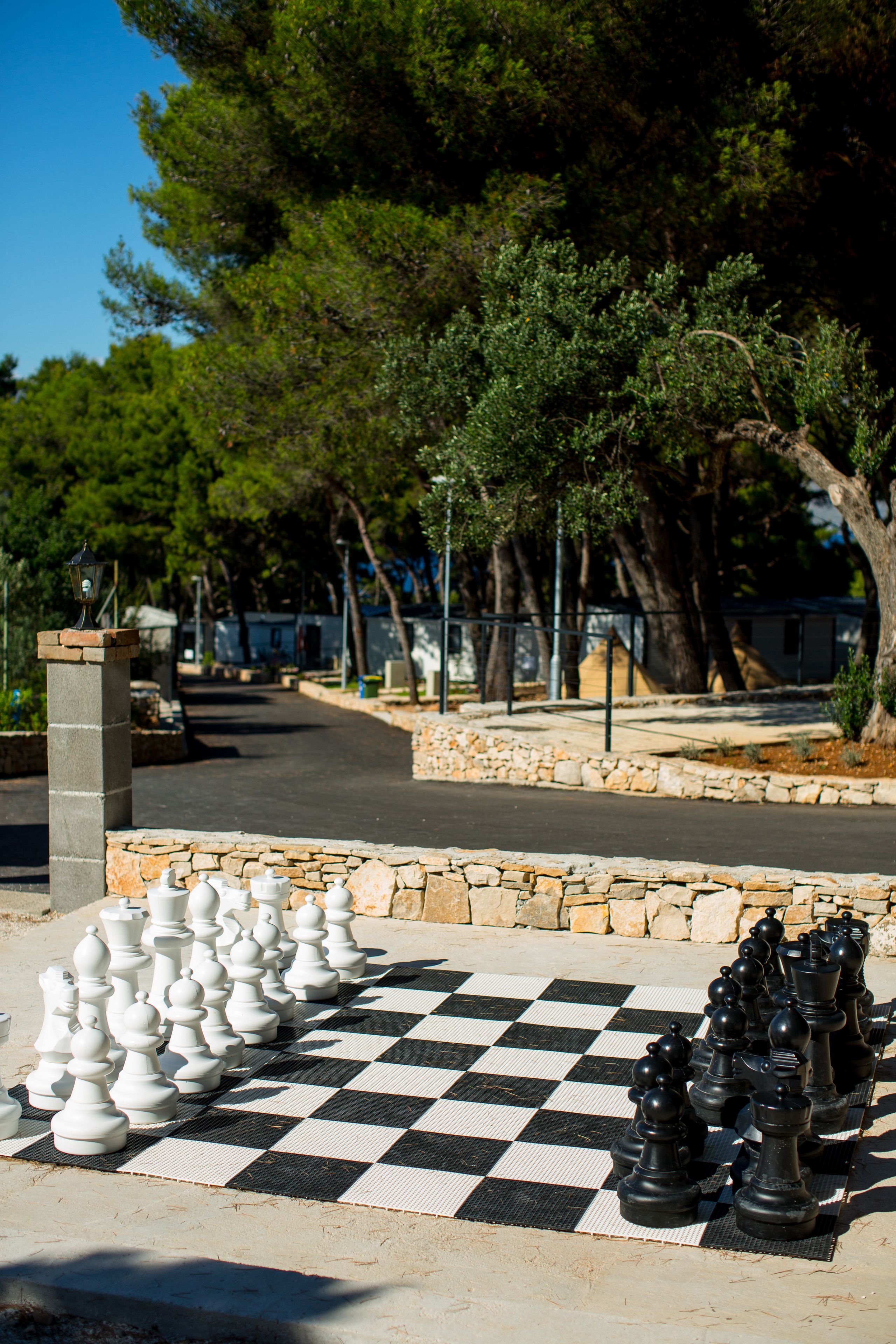 A chessboard with pieces set up outdoors, surrounded by a stone wall and trees.