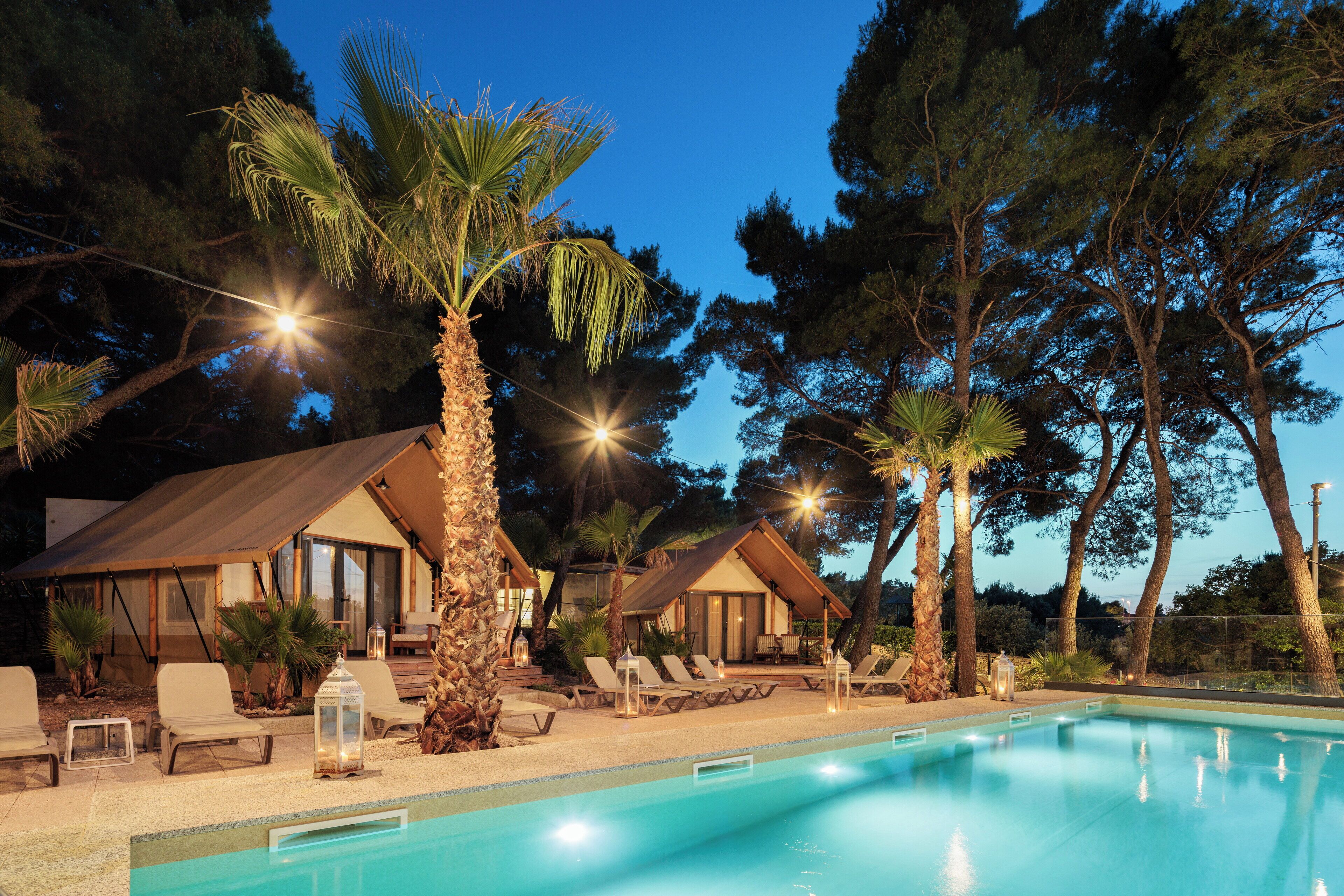 A pool area with lounge chairs, palm trees, and a building with a sloped roof.