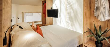 A bedroom with a bed, a TV, a plant, and a wooden wardrobe.