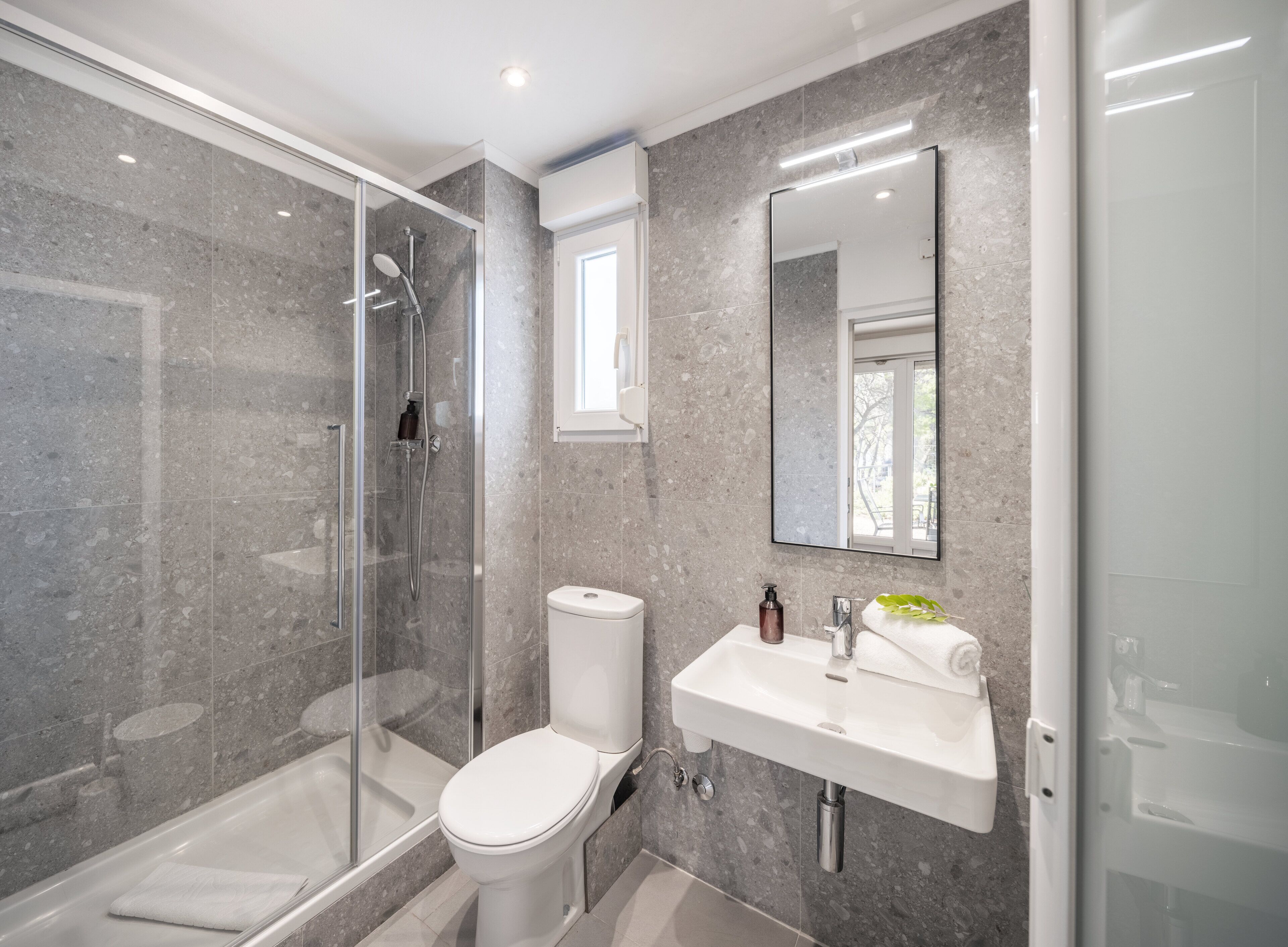A modern bathroom with a glass-enclosed shower, a white toilet, and a sink with a mirror above it.