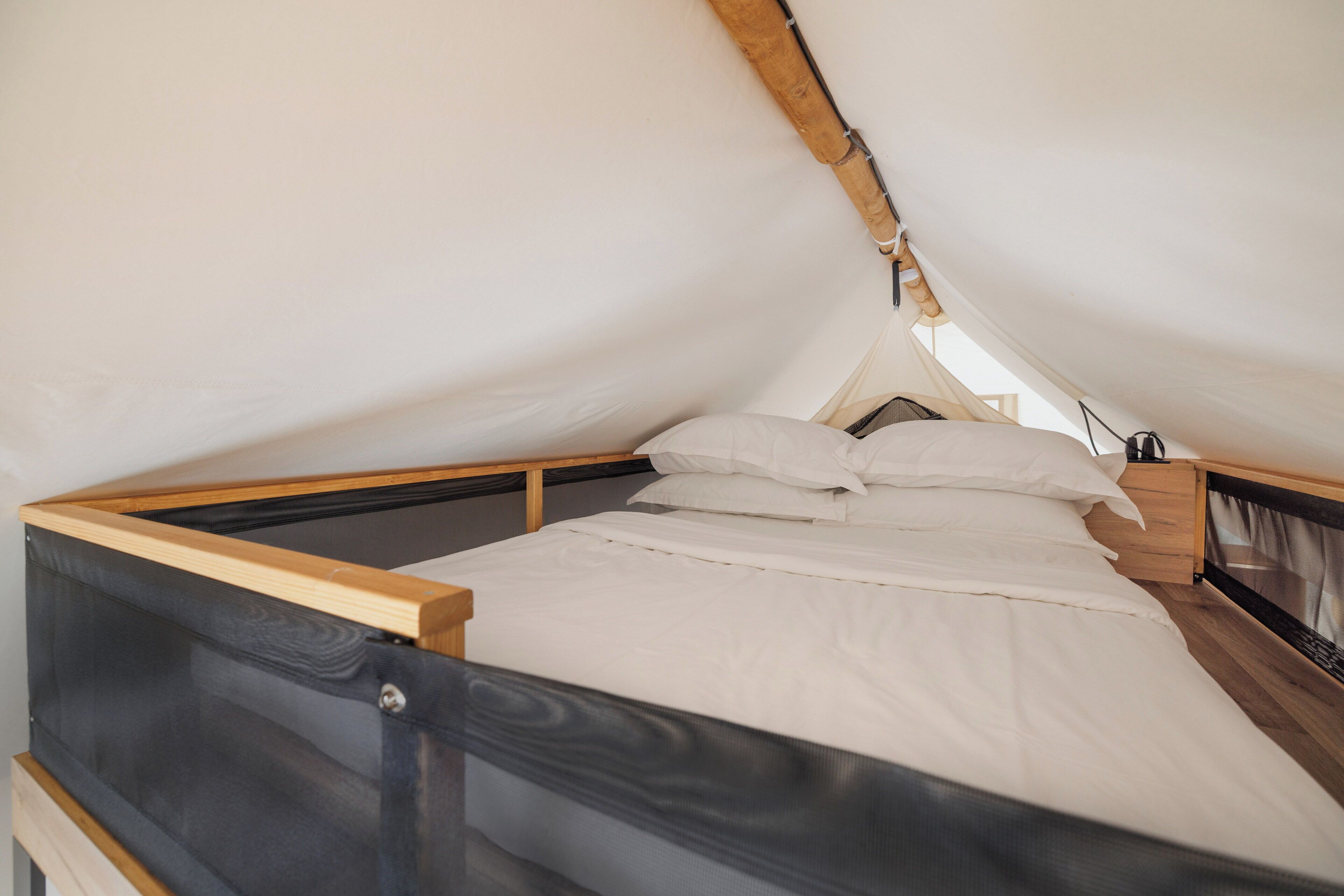 A single bed with white bedding in a tent-like structure with wooden beams.