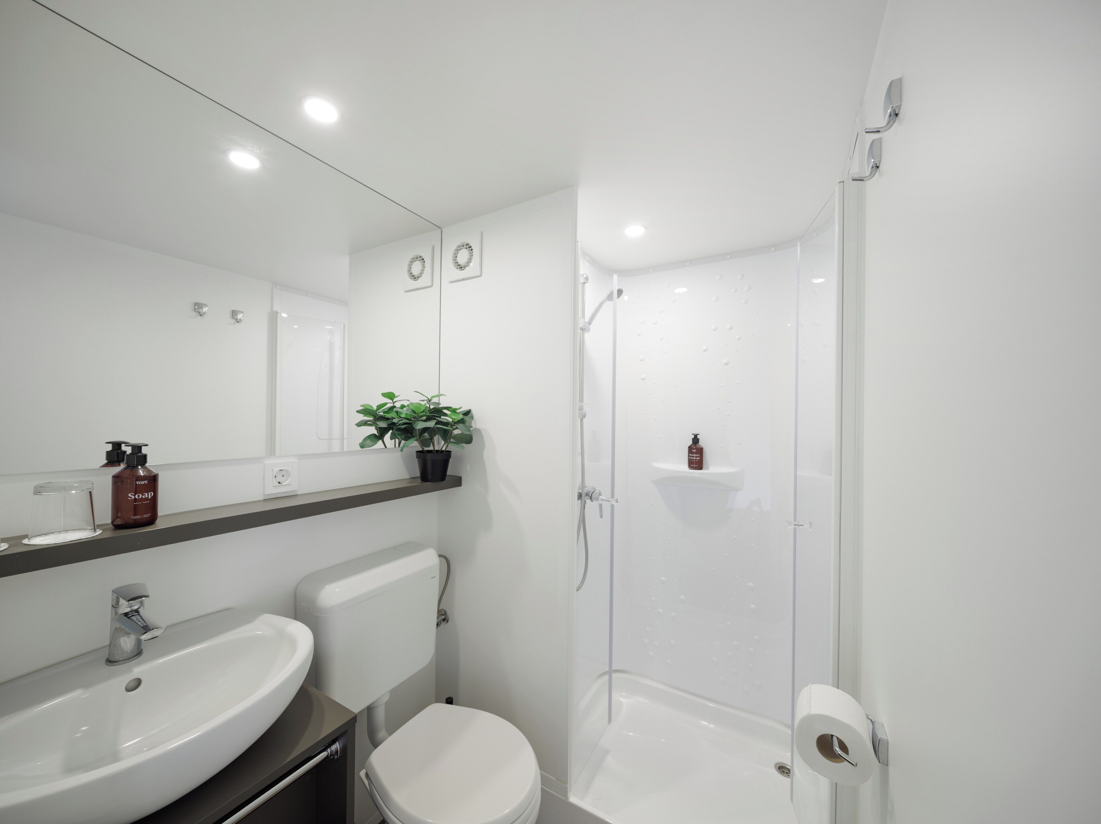 Une salle de bain moderne avec un lavabo blanc, des toilettes et une douche à parois de verre.