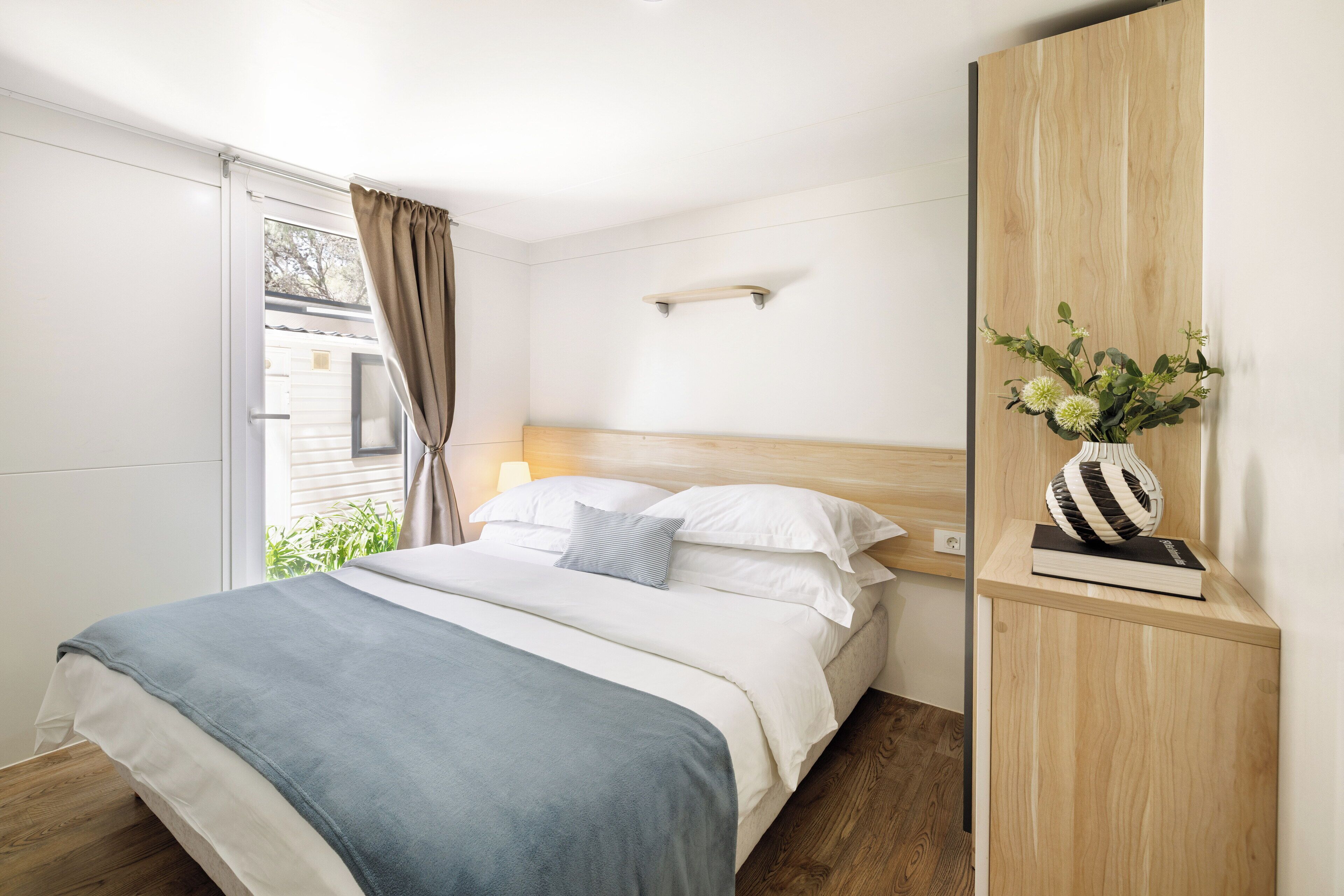 A neatly made bed with a blue blanket, a wooden headboard, and a bedside table with a vase of flowers.