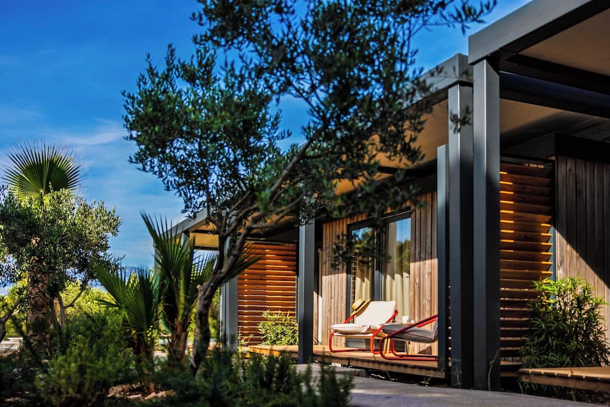 A modern house with a wooden exterior, a covered outdoor seating area, and lush greenery.