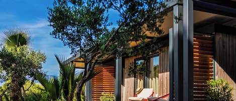 Une maison moderne avec une façade en bois, un espace extérieur aménagé et abrité, et une végétation luxuriante.