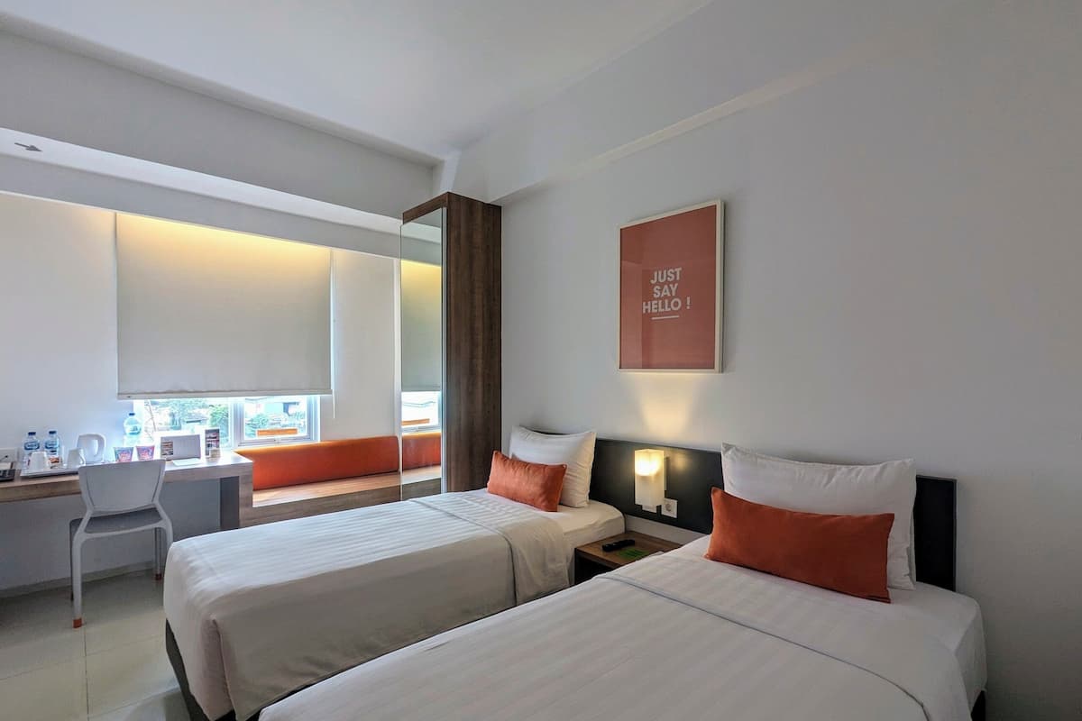 A hotel room with two beds, a desk, and a window with a view.