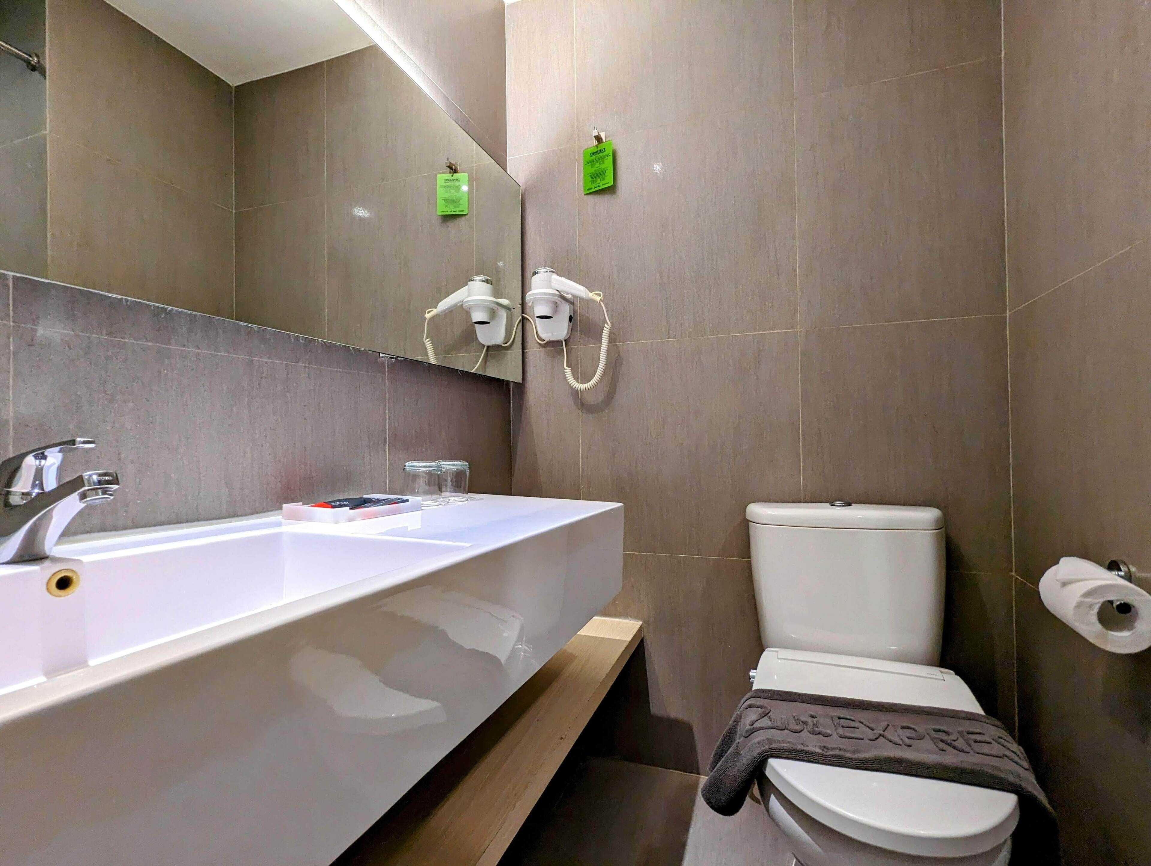 Un baño moderno con un lavamanos grande blanco, un inodoro y un espejo sobre el lavamanos.