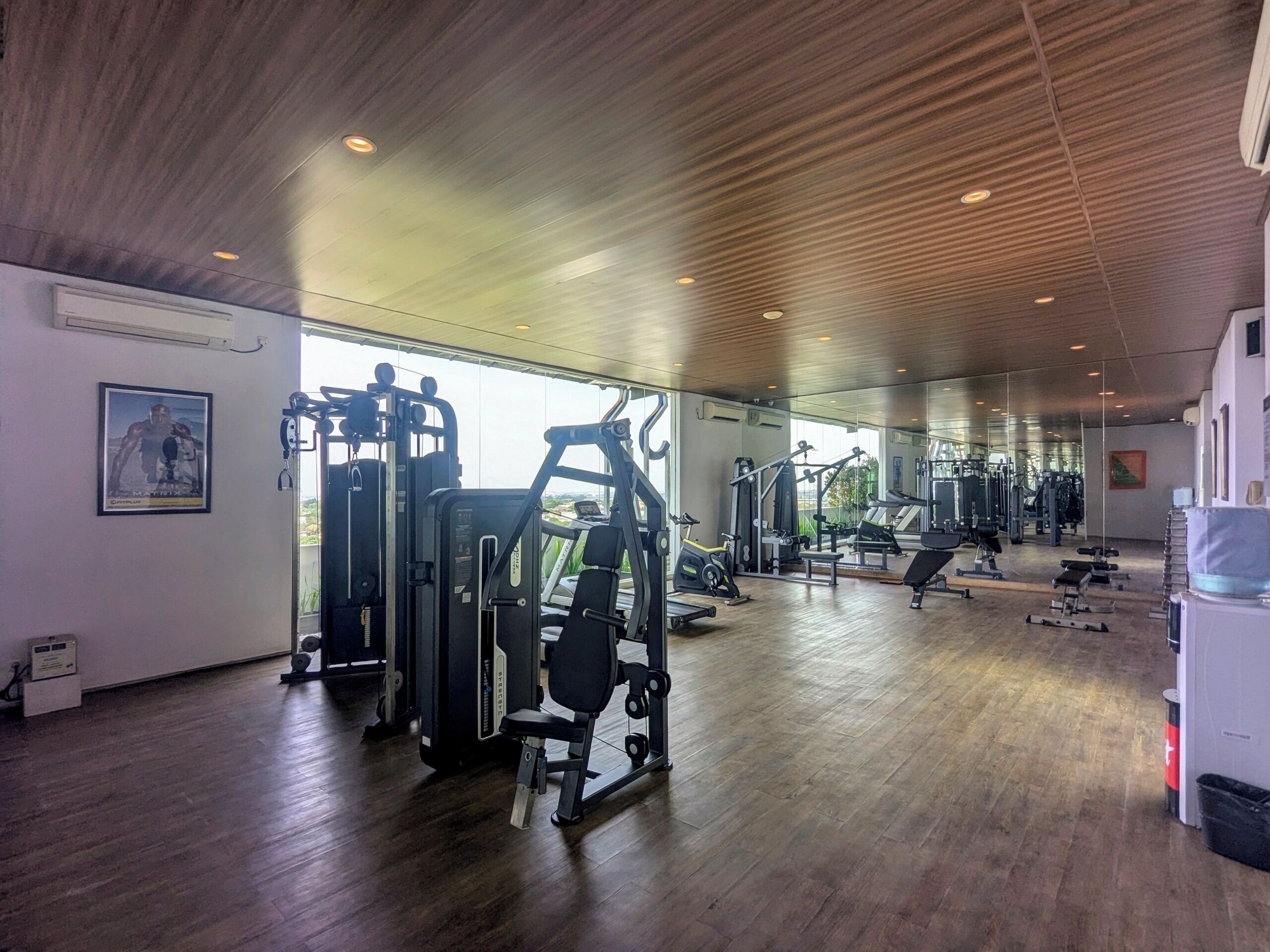 A spacious gym with various exercise machines, a wooden ceiling, and large windows.