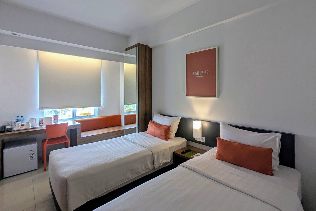 A hotel room with two beds, a desk, a chair, and a large window.