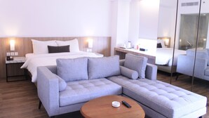 A modern hotel room with a bed, a grey sofa, a wooden coffee table, and a large mirror. - Zuri Express Lippo Cikarang (Bekasi)