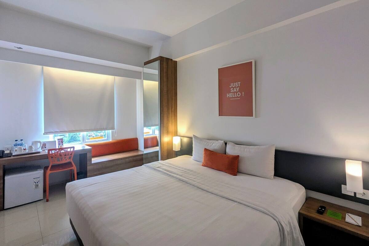 A modern hotel room with a large bed, a desk, and a window with a view.