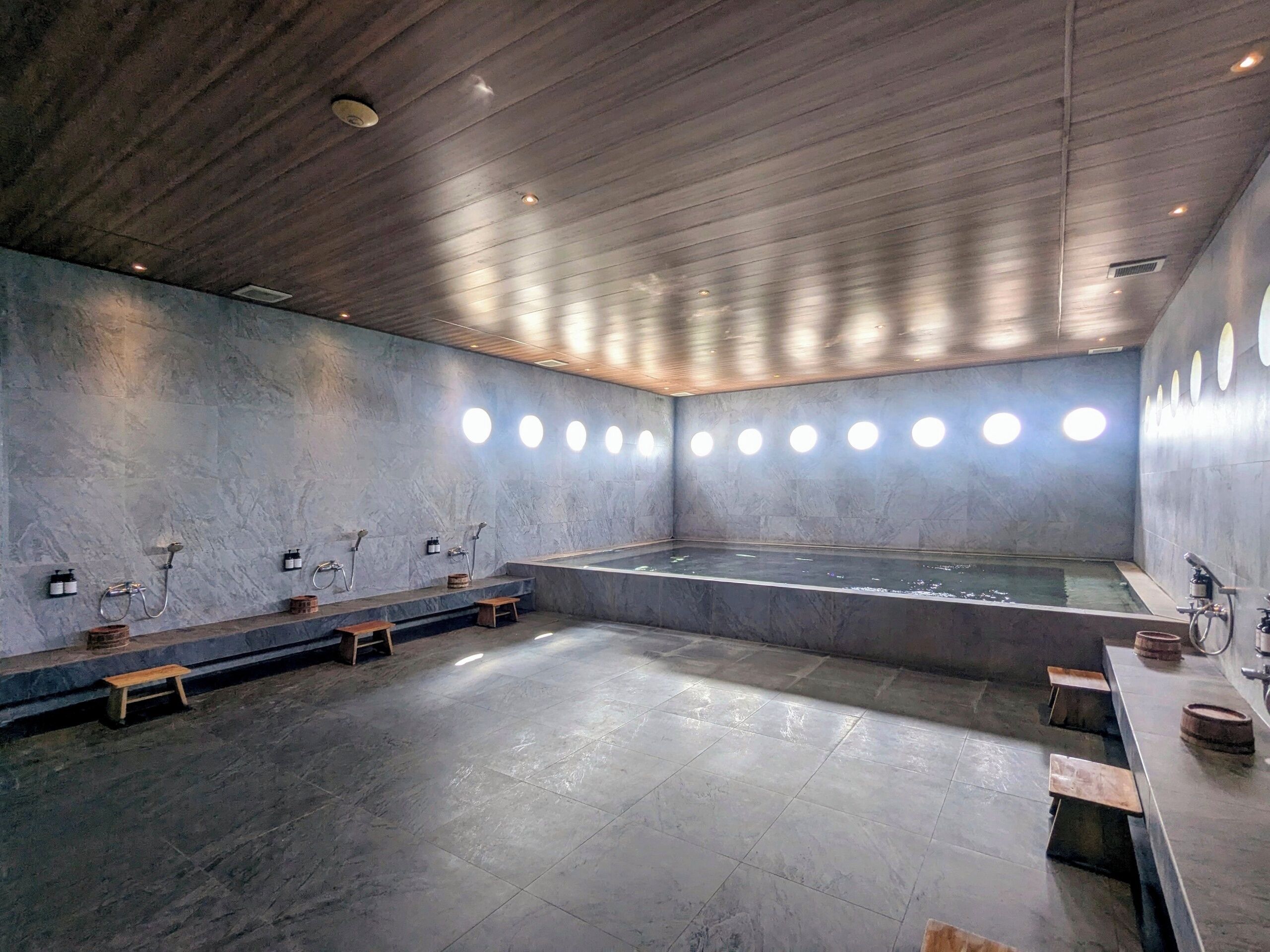 Un spa moderno con una bañera grande, bancos de madera y una pared de piedra.