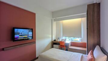 A hotel room with a bed, a desk, a chair, a television mounted on the wall, and a window with a view.