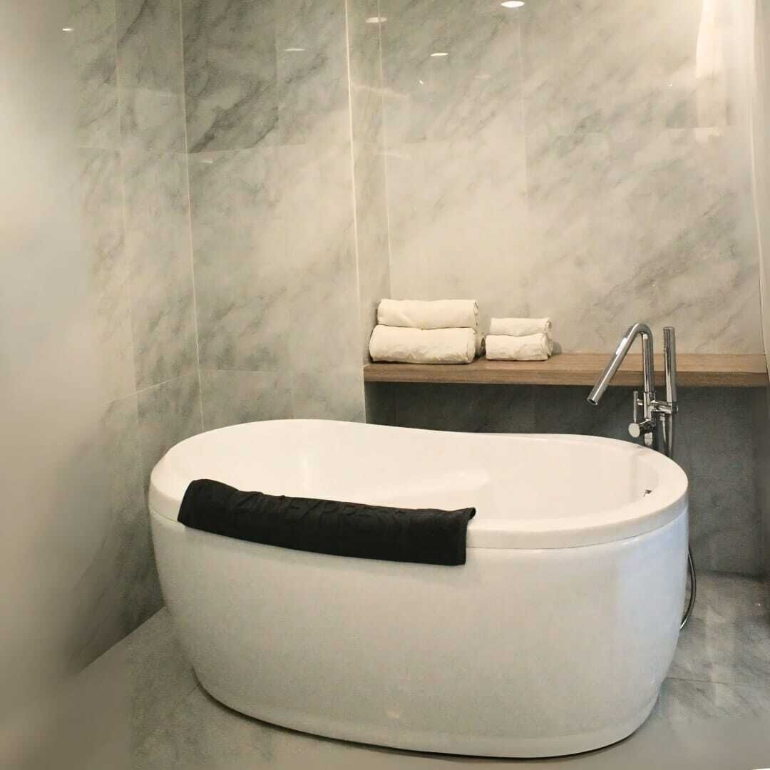 Un baño moderno con una bañera independiente, un estante empotrado con toallas y una pared de mármol.