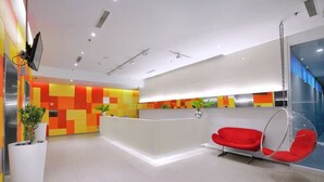 A modern reception area with a colorful wall design, a white reception desk, and red chairs.