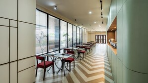 A modern dining area with long tables and chairs, large windows, and a chevron-patterned floor.