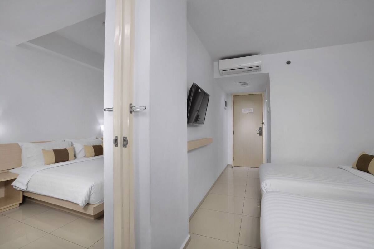 Quarto de hotel com duas camas, televisão e aparelho de ar condicionado.