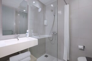 Un baño moderno con ducha envuelta en vidrio, un lavamanos blanco y un inodoro.