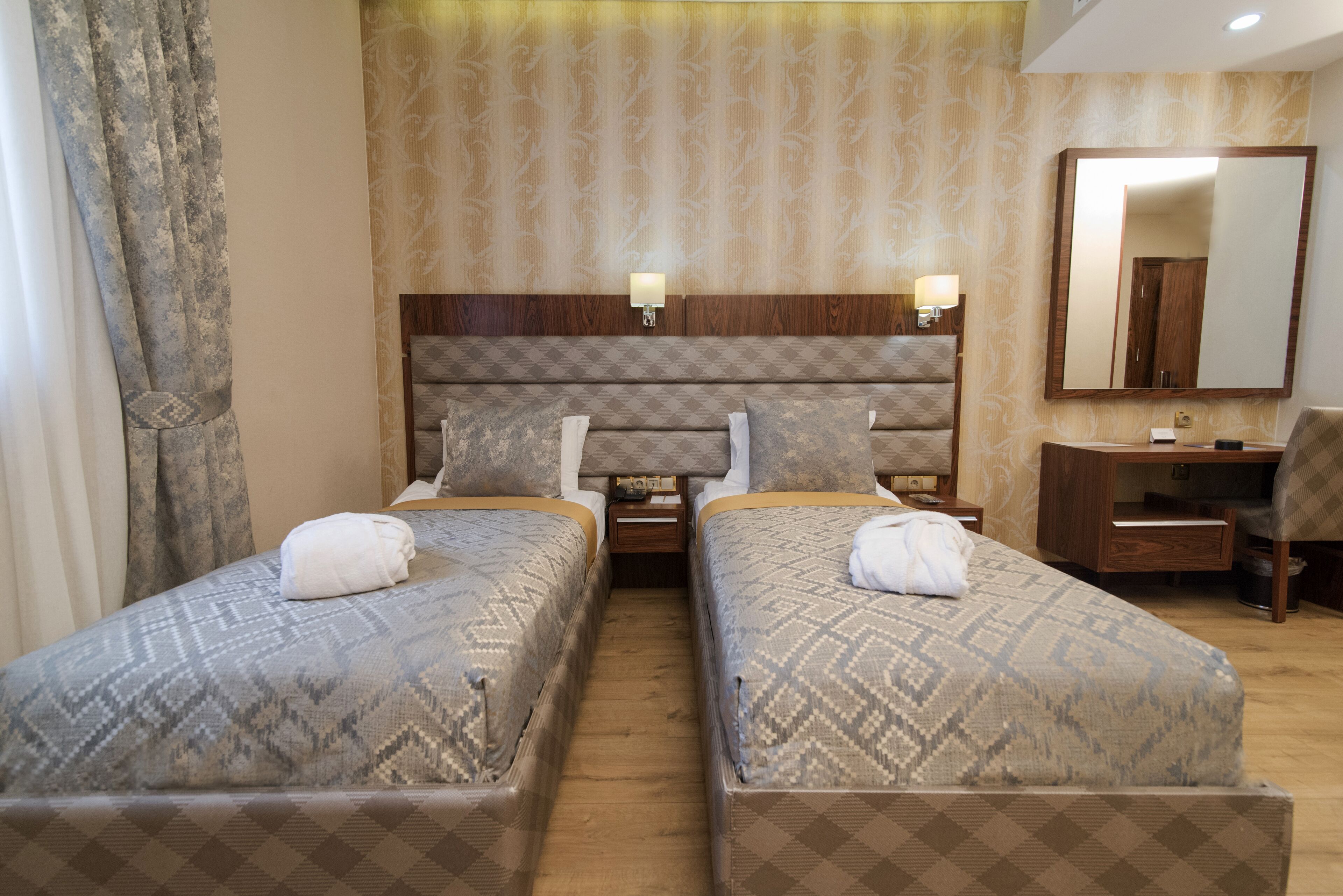 A hotel room with two beds, a wooden headboard, a desk, a chair, and a mirror.