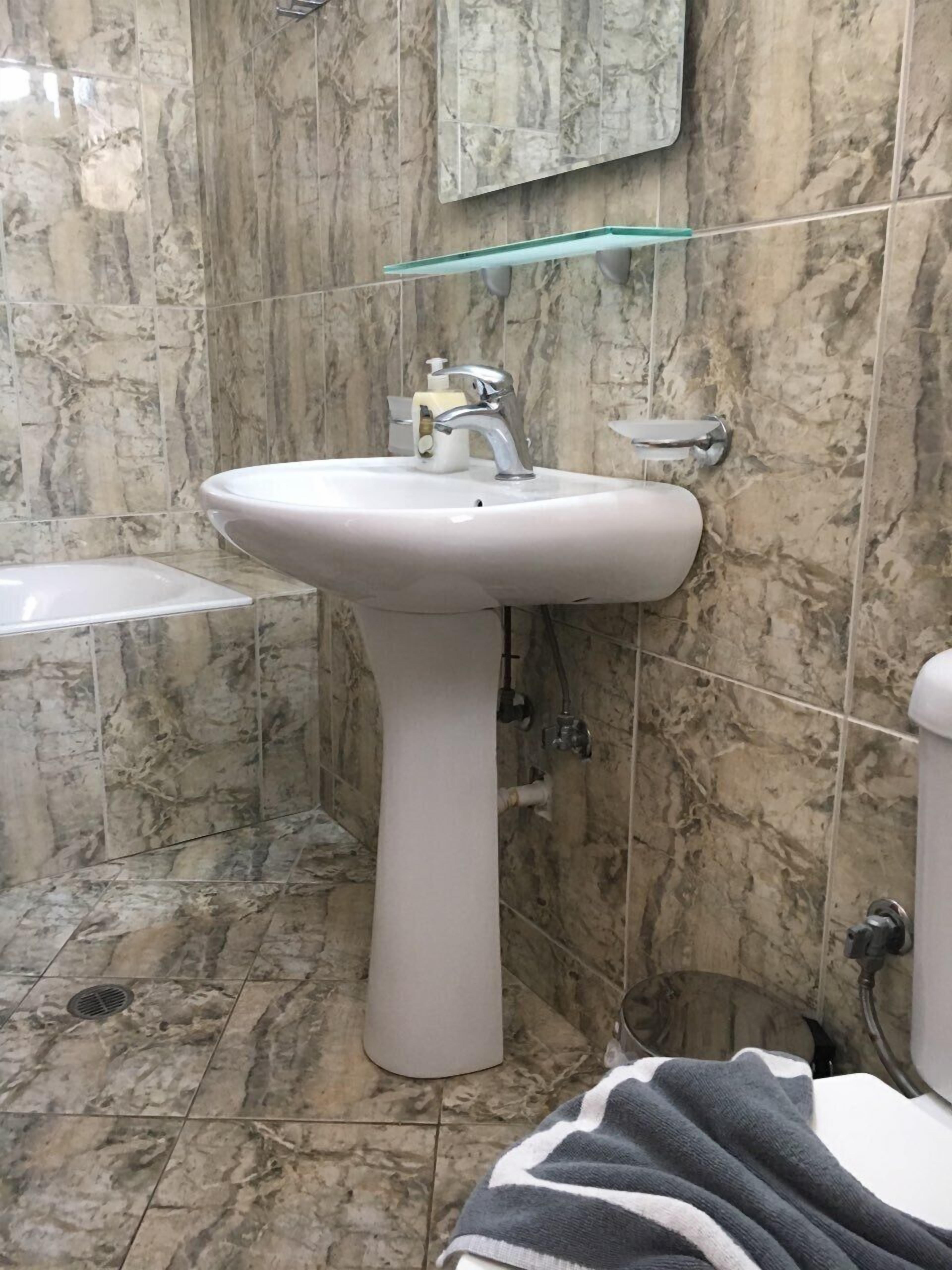 A bathroom with a pedestal sink, a mirror above it, and a towel on the floor.