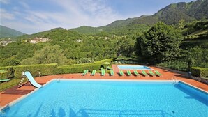 A swimming pool with multiple lanes and a slide, surrounded by lush greenery and mountains in the background. - Residence Casa Gardola (Tignale)
