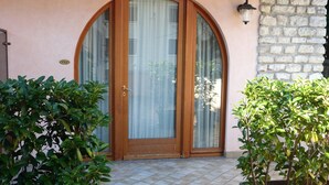 A house with a large arched wooden door, a tiled entrance, and potted plants on either side. - Residence Casa Gardola (Tignale)