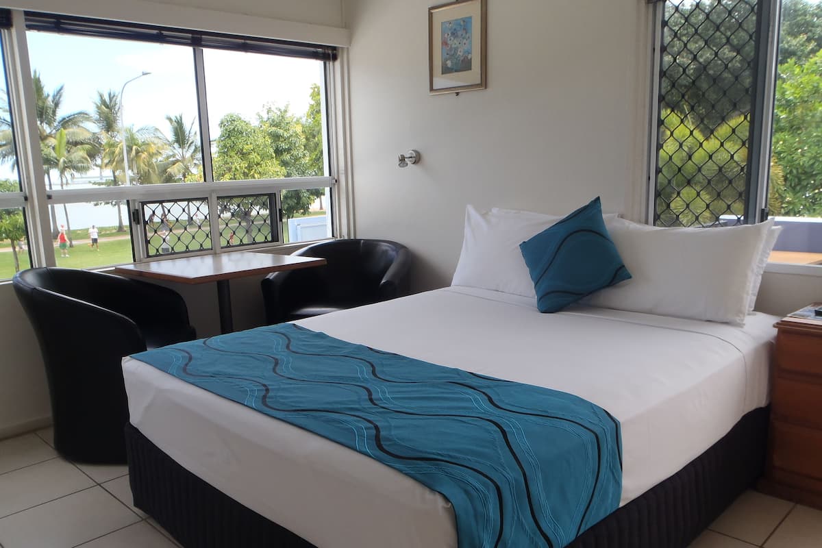 Une chambre d’hôtel avec un lit, un bureau, une chaise et une vue sur les palmiers par la fenêtre.