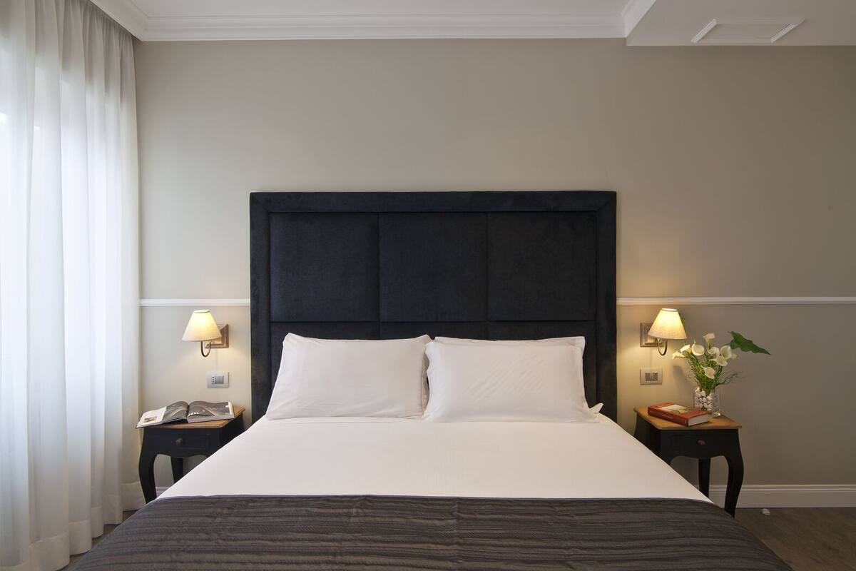 A neatly made bed with a dark headboard, two bedside tables with lamps, and a vase with flowers on one of the tables.