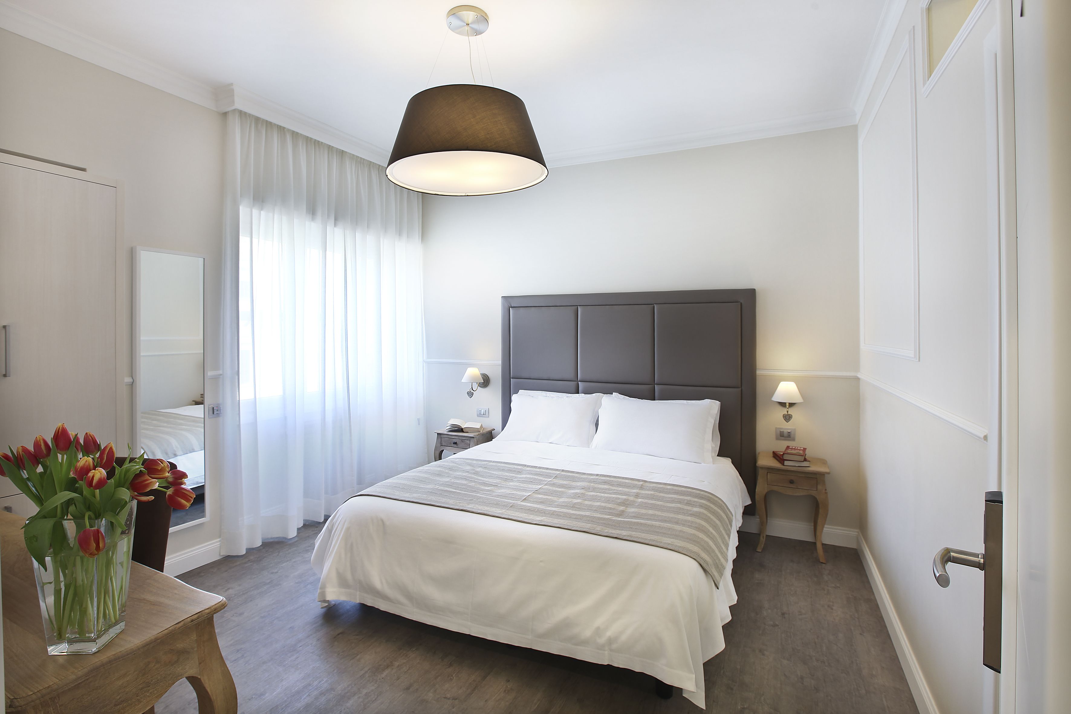 Camera d'albergo con un letto grande, comodini, un tavolino e un vaso di fiori, con vista all'esterno dalla finestra.