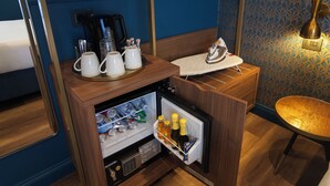 A compact minibar with a refrigerator, a coffee maker, and a small table with a towel and an iron.