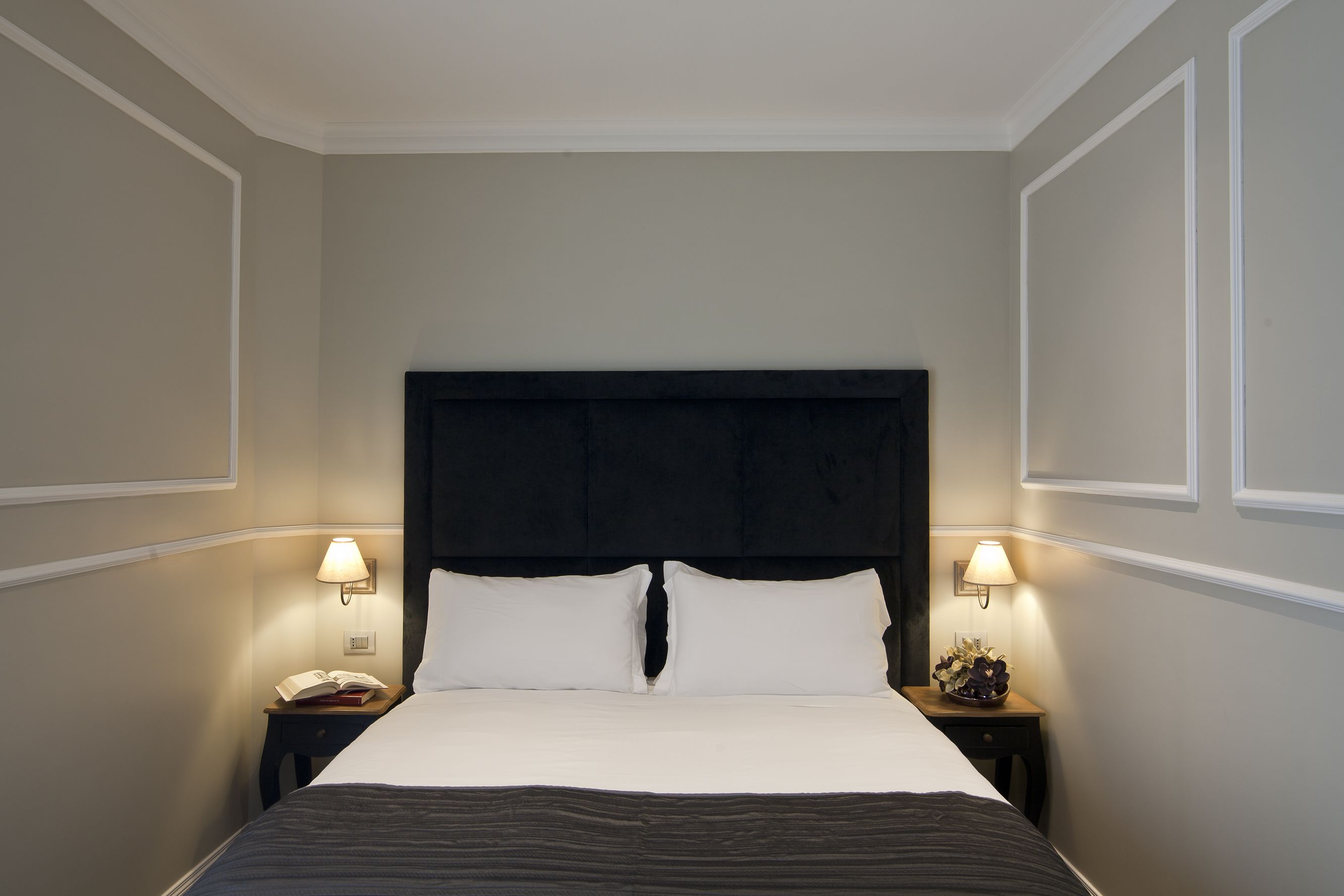 A neatly made bed with a dark headboard, two bedside lamps, and a small bedside table with a lamp and a decorative item.