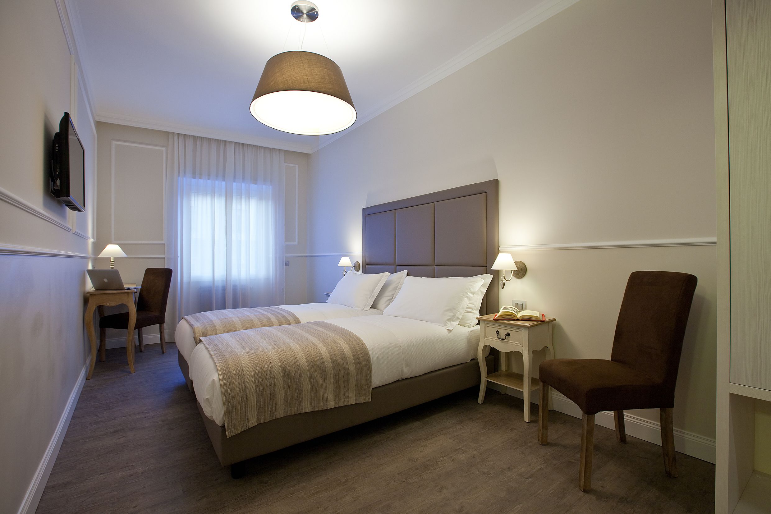 A hotel room with a bed, a desk, a chair, and a TV.